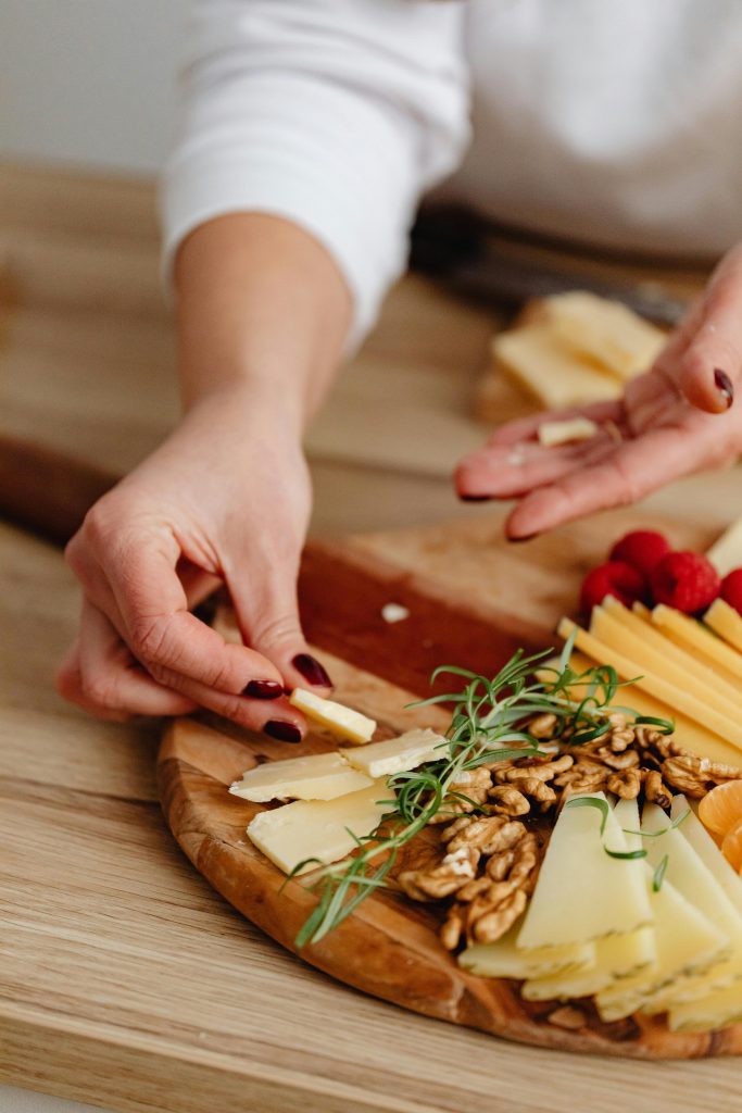 Close-up of hands arranging a cheese and nut charcuterie board.